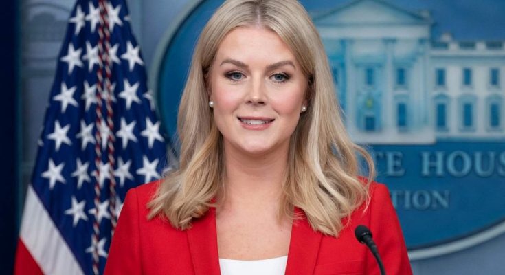 karoline Leavitt at White House press briefing podium wearing red blazer, American flag