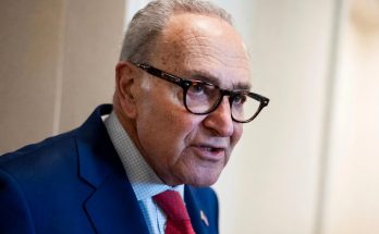 man in blue suit speaking passionately indoors, wearing glasses